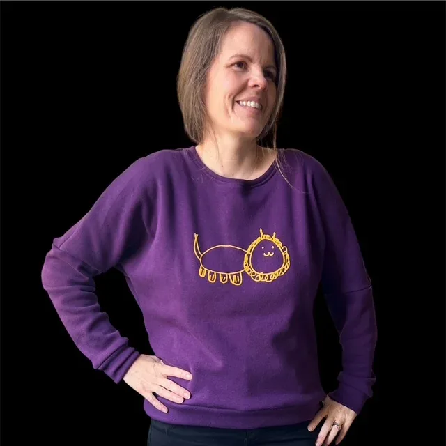 Romi trägt einen violetten Pullover mit der gelben Löwenzeichnung ihrer Tochter